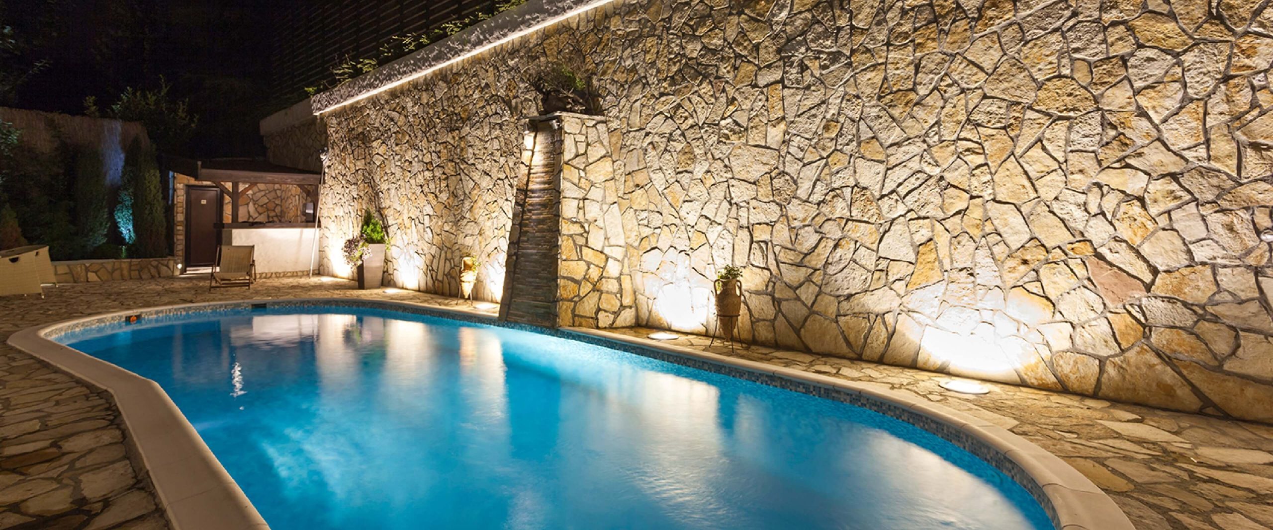 Bild eines Pools mit einer beleuchteten Natursteinmauer dahinter