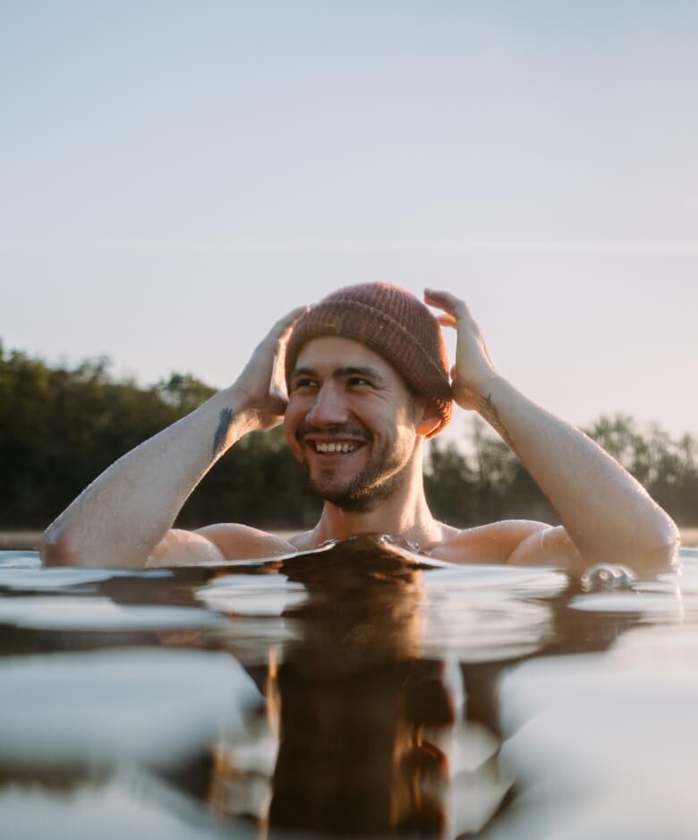 Bild eines lächelnden Mannes der mit Wollmütze in einem Poolbecken steht