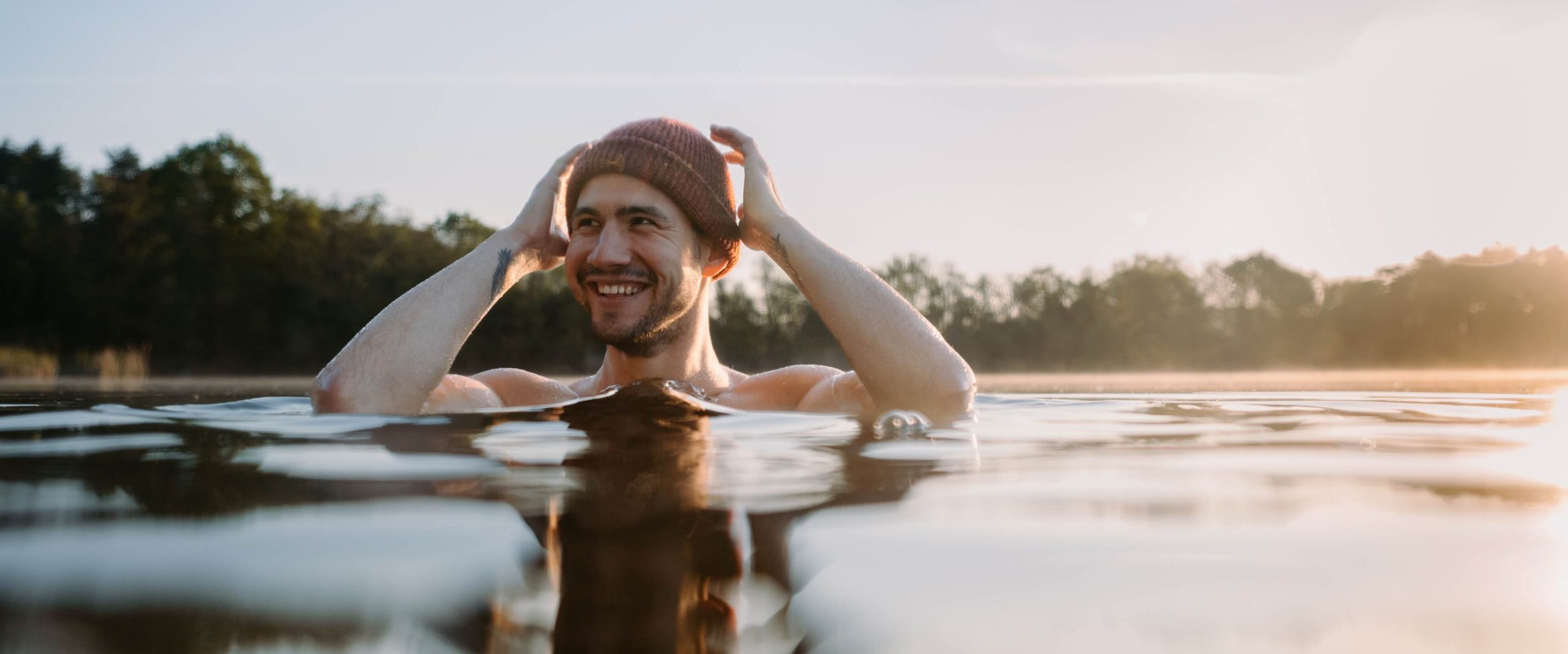 Bild eines lächelnden Mannes der mit Wollmütze in einem Poolbecken steht