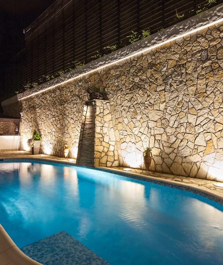 Bild eines Pools mit einer beleuchteten Natursteinmauer dahinter